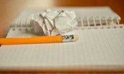 Un crayon machouillé est posé sur un cahier à côté d'une feuille chiffonnée.